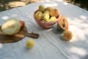 Fruits including a melon, apples, and a papaya on a white cloth outdoors.