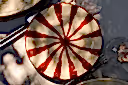 A round glass plate with a cream-colored base and a red radial starburst pattern, styled on a gray table with silver cutlery and other dining items.
