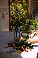 Person arranging flowers on a table with a vase in the background